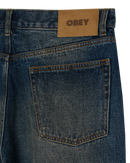 Obey Classic Baggy Denim Oil Stained Indigo, denim jeans van 100% cotton met shank button closure, button fly en 5-pocket styling, relaxed fit straight leg, taillemaatjes 28-38, verkrijgbaar bij Revert 95 Haarlem
