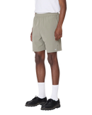 Obey Travel Short in Vetiver, 92% polyester 8% spandex 3.5 oz lichtgewicht short met elastic waistband rounded drawcord faux fly front slash pockets zipper closure back welt pocket reflective Obey logo op been relaxed fit 7 inch inseam in gedempte olijfgroene Vetiver colorway, verkrijgbaar bij Revert 95 Haarlem